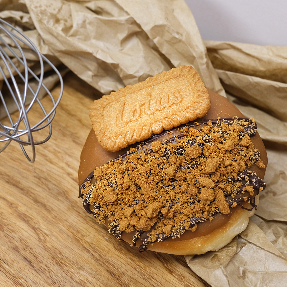 A single lotus biscoff doughnut with a lotus biscuit on top next to a whisk in a Newbury bakery