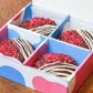 Box of chocolate-dipped treats with red sprinkles on a wooden surface