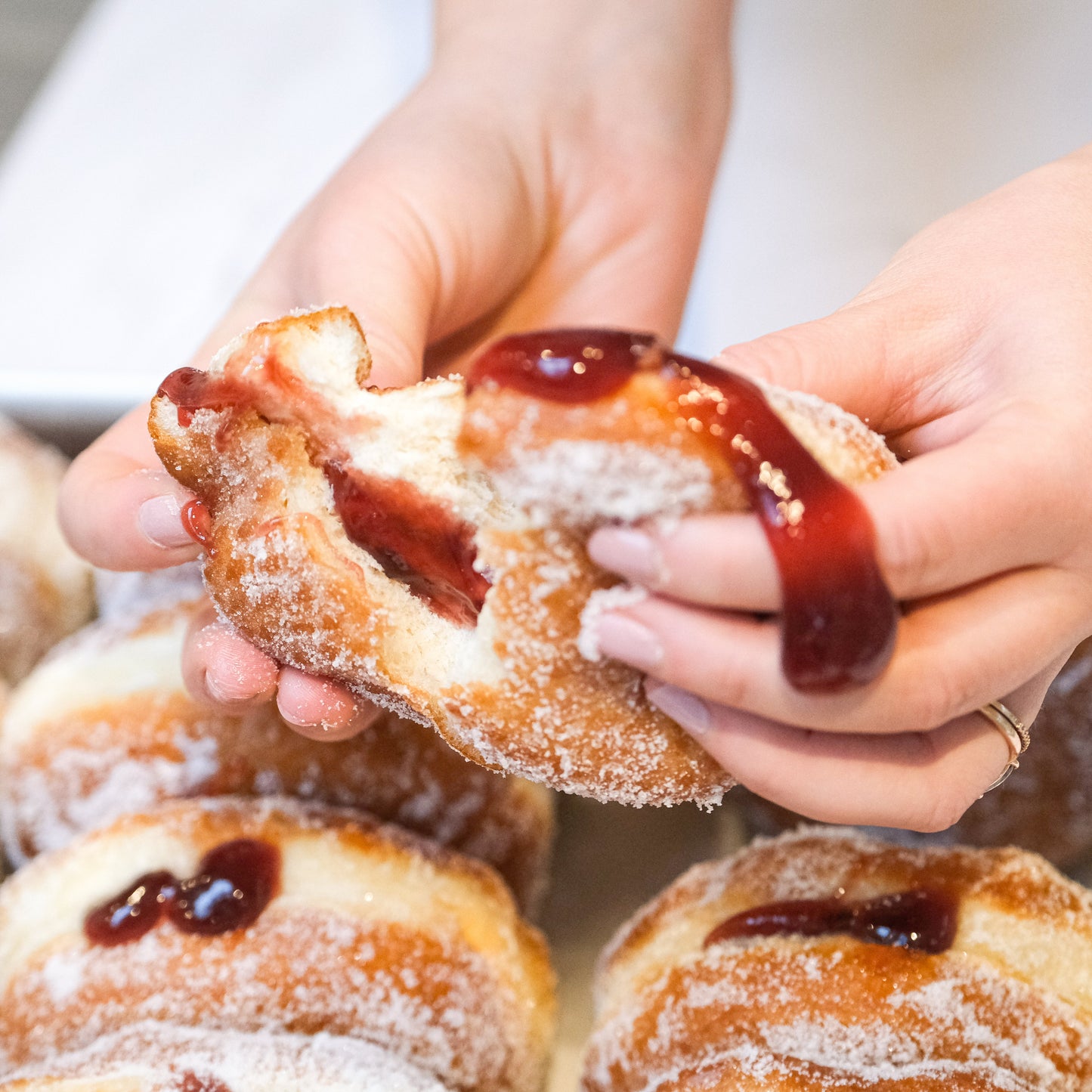 Person holding a jelly-filled donut with more donuts in the background