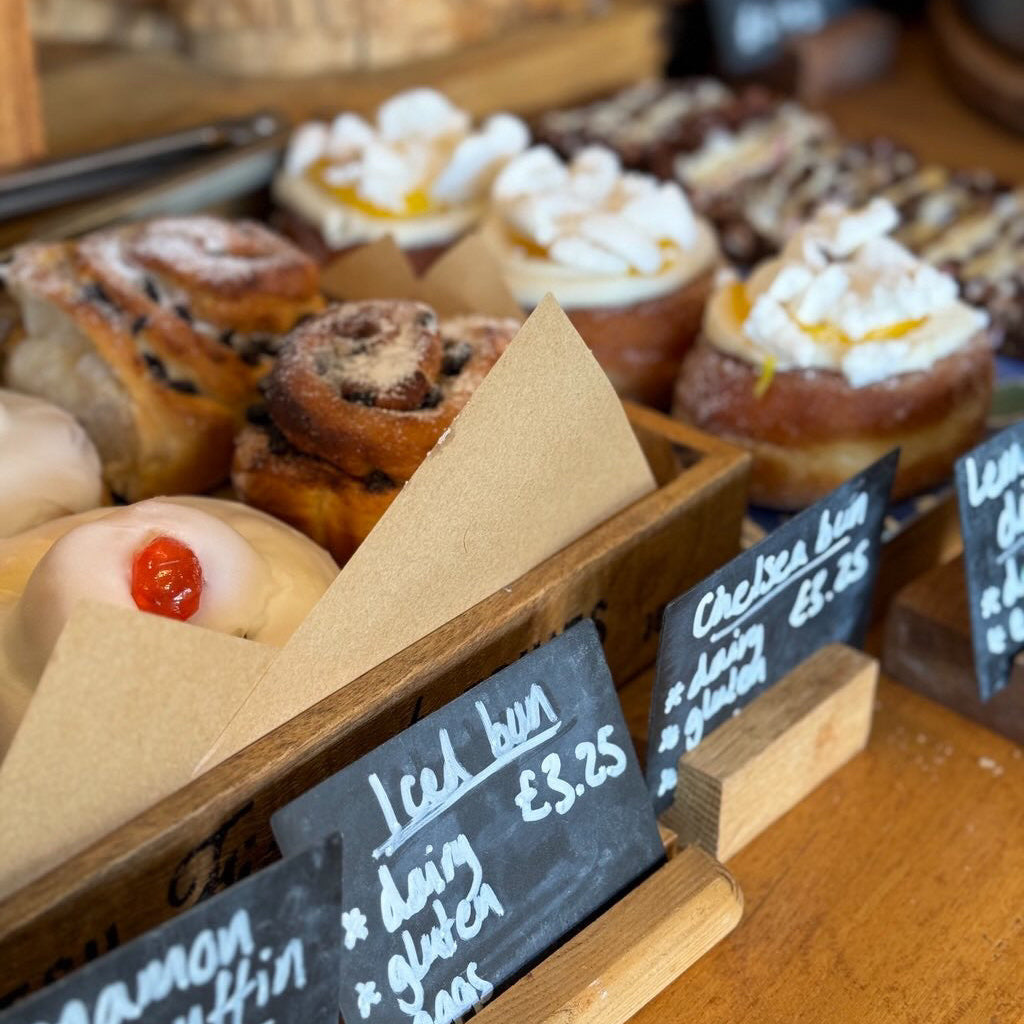A display of sweet treats including iced buns and doughnuts with chalkboard labels