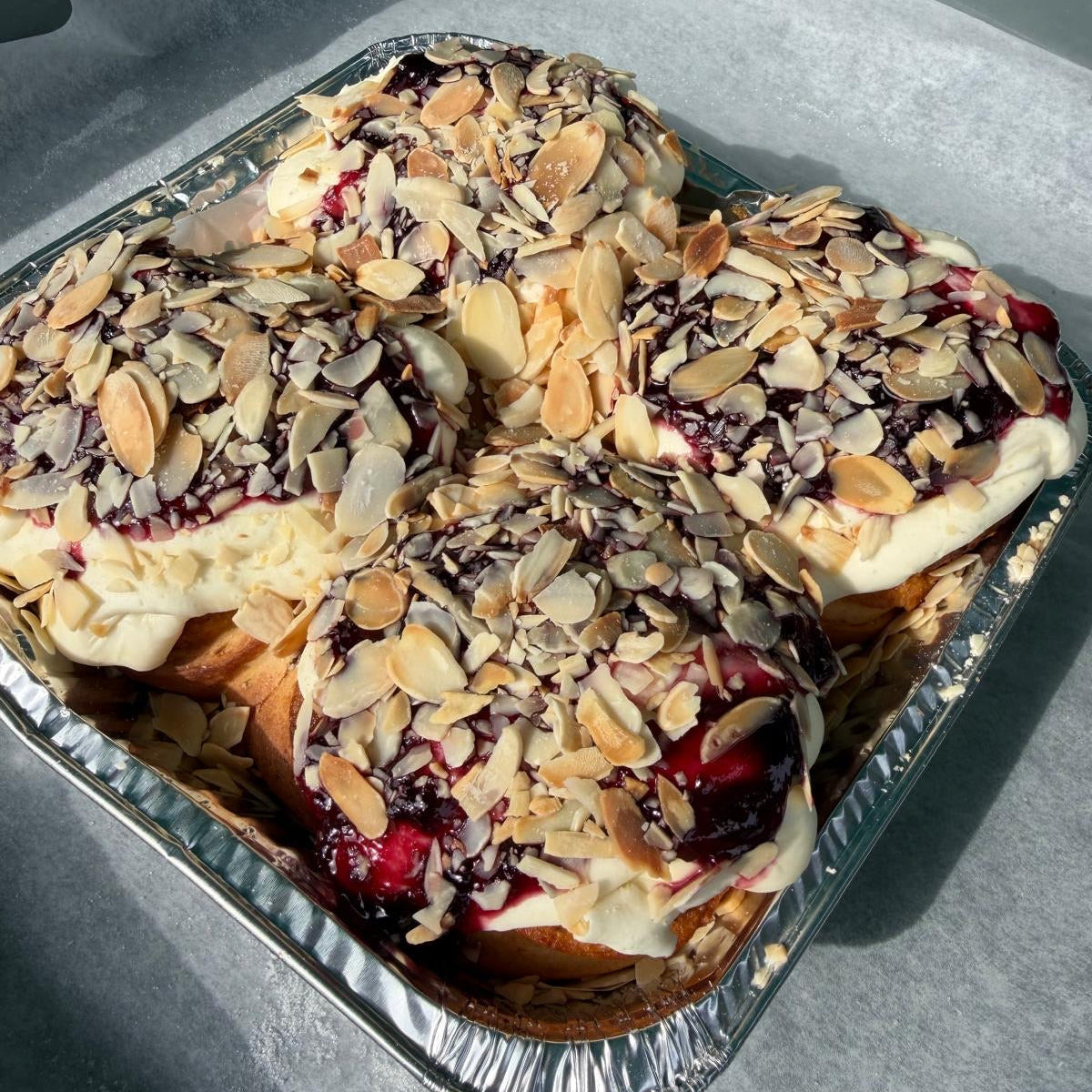 Almond and berry pastry rolls in a square aluminum tray lined with parchment paper.