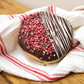 A chocolate topped doughnut with a drizzle and raspberry pieces