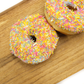Two ring doughnuts covered in colourful sprinkles on a wooden chopping board