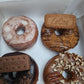 A box of vegan doughnuts with various toppings including a bourbon biscuit, lotus biscoff and pecan nuts.